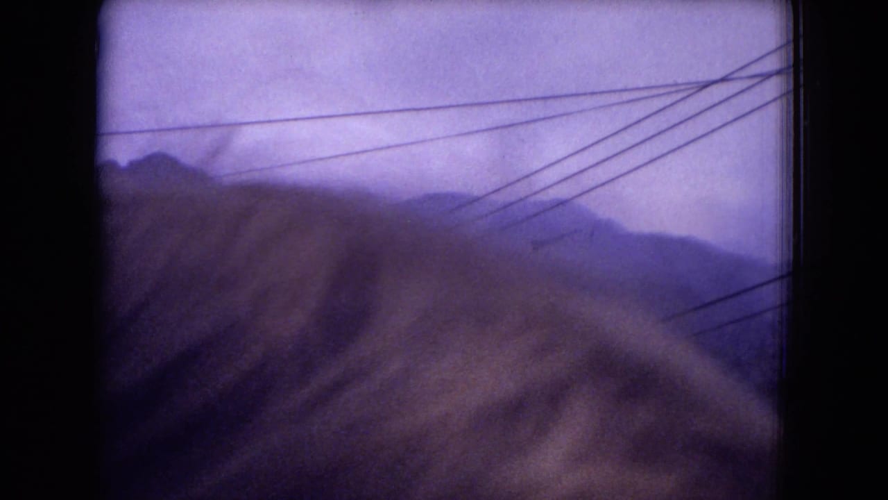 1973 8mm view of hazy Gila National Forest mountain ridges with power lines crossing the sky and a soft foreground blur.