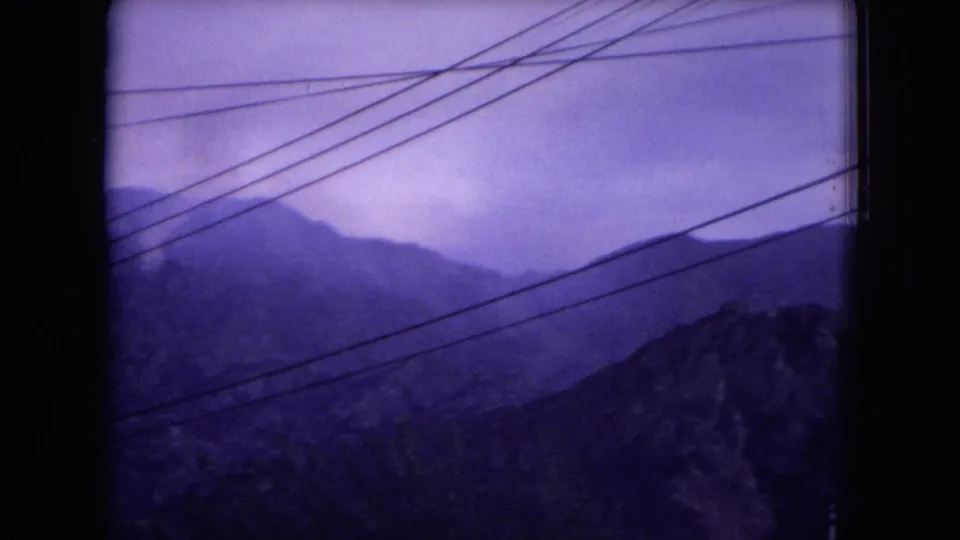 Final 1973 8mm frame of New Mexico mountain ridges, purple-tinted sky, and utility lines viewed from a roadside or window perspective.