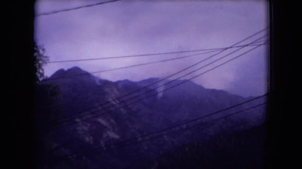 Soft 8mm view of layered Gila-area mountain peaks with several overhead power lines crossing the foreground.