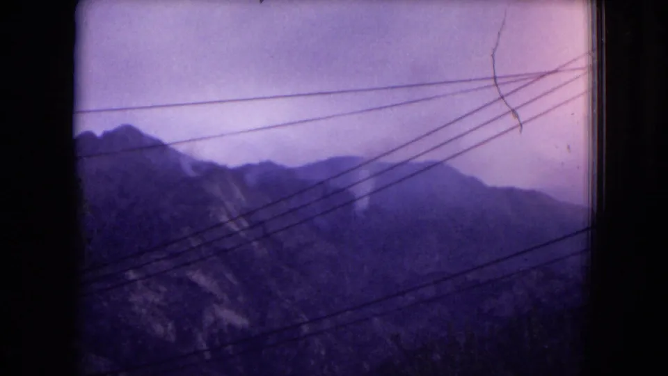 Final purple-tinted frame showing a distant New Mexico mountain range beneath a pale sky, with power lines crossing the view.