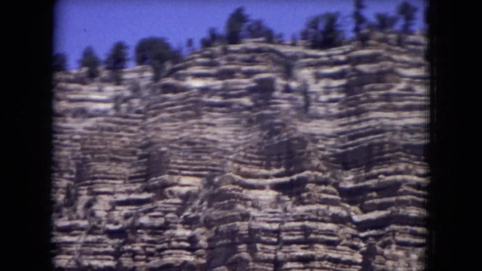 1973 home-movie frame of striated New Mexico cliff faces, tightly framed with visible grain and slight motion blur.