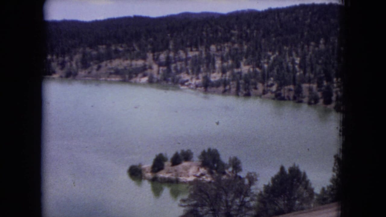 Elevated view of a calm lake with a small tree-covered island and forested hills beyond.