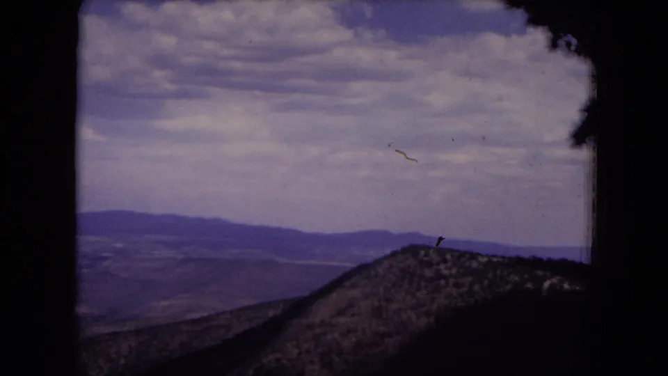 Gila National Forest landscape on 8mm film, showing a rounded foreground slope and layered distant ridges beneath scattered clouds.