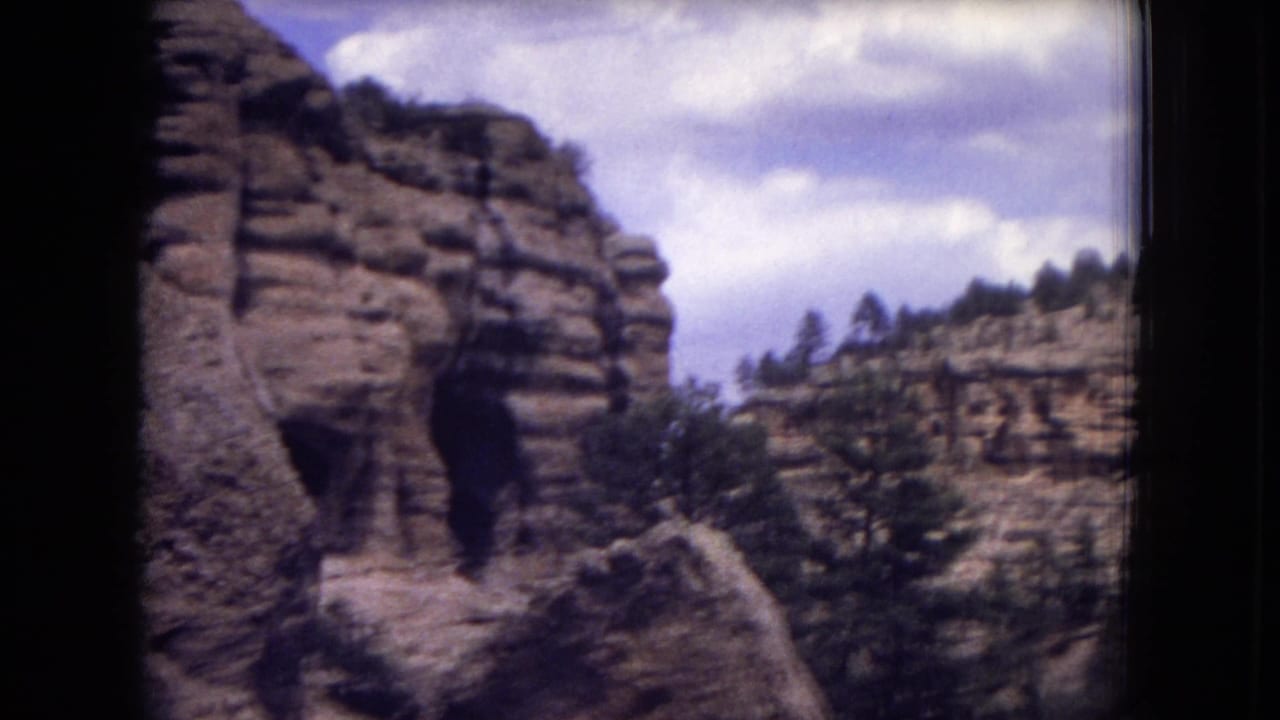 Rocky canyon wall and distant pine-covered ridge beneath clouds.