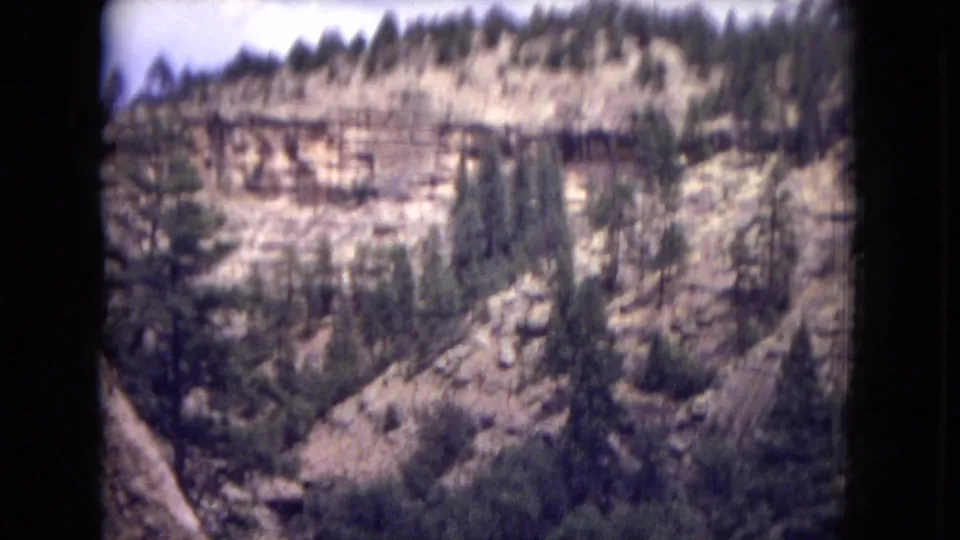 1973 8mm home-movie view across pale canyon cliffs and pine-covered slopes in Gila National Forest, New Mexico.