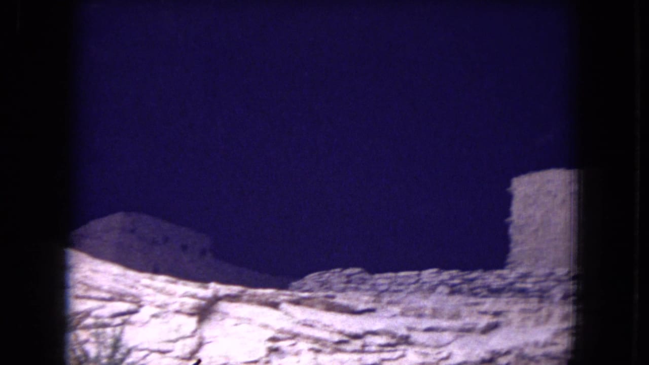 1973 8mm frame from Gila National Forest showing weathered stone ruin walls on pale rock beneath a deep blue sky.