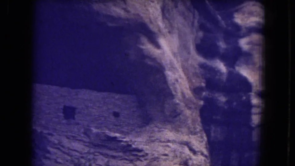 Close 8mm view of a masonry wall beside sculpted sandstone rock, likely part of the Gila National Forest ruins shown in the clip.