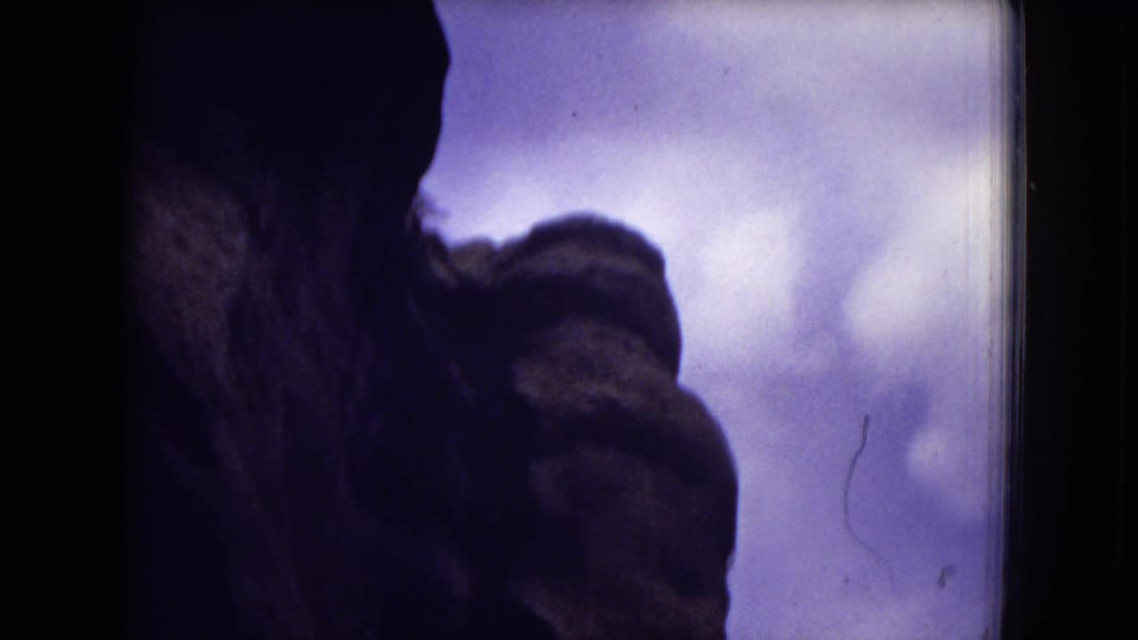 1973 8mm frame from Gila National Forest showing a shadowed rock formation silhouetted against a purple-toned sky.