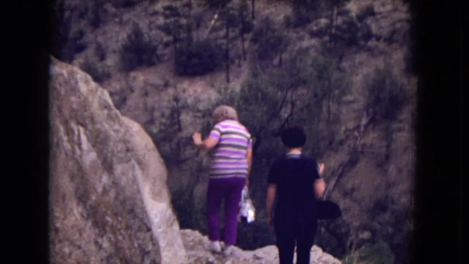 Two women hiking among large rocks in Gila National Forest, with one wearing purple striped clothing and the other in dark clothing.