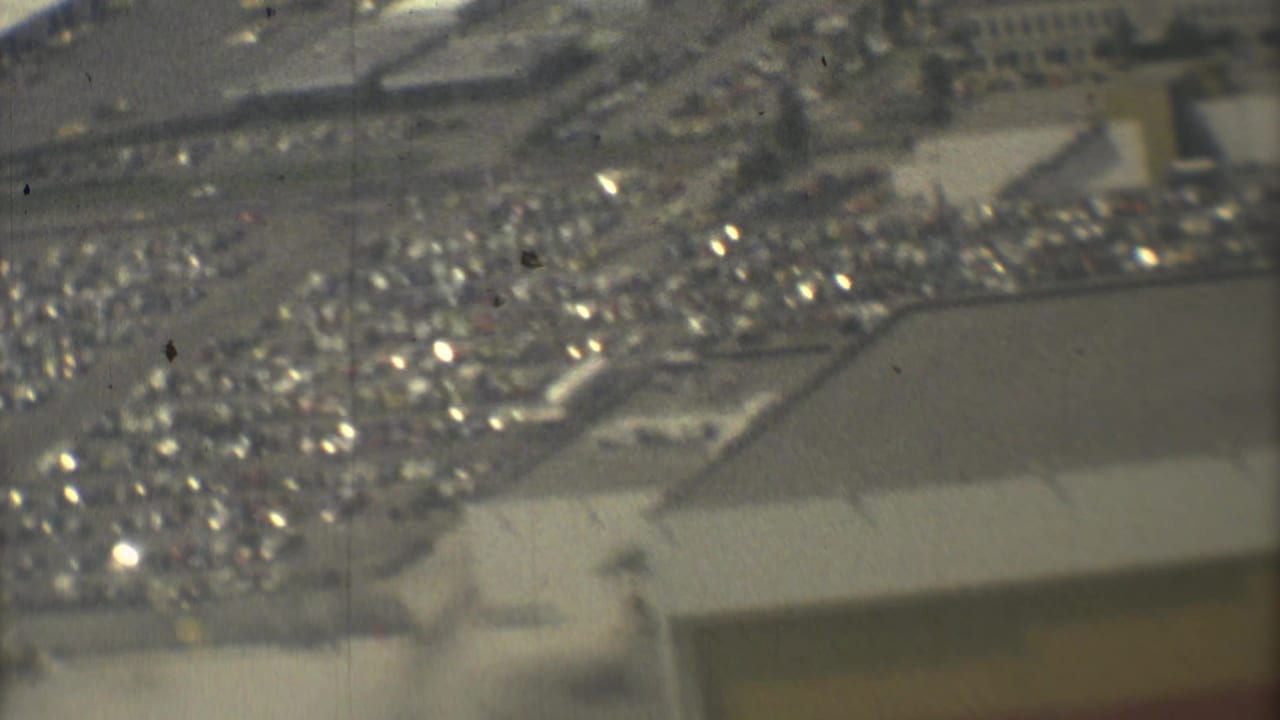 1973 Mexico City aerial footage looking down toward a busy airport parking lot and adjacent paved airport area.