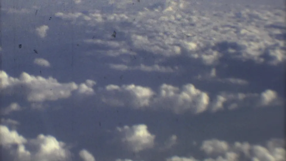 The Mexico City airport view gives way to a 1970s 8mm aerial cloudscape with blue sky and scattered white clouds.