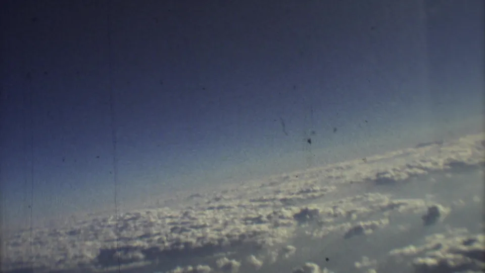 A soft 8mm frame of cloud tops and blue sky during a 1973 airplane flight associated with Mexico City travel footage.