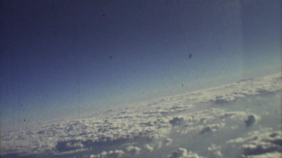Faded 1973 8mm airplane-window view of bright clouds, pale sky, and visible film texture from the Mexico City travel clip.