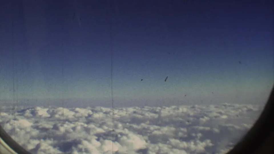 1973 8mm airplane-window view with a curved window edge framing clouds and blue sky above the Mexico City travel route.