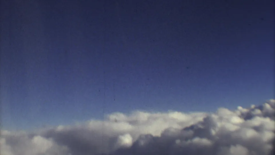 8mm aircraft-window view from 1973, focused on bright cloud tops beneath a dark blue sky with visible archival film wear.