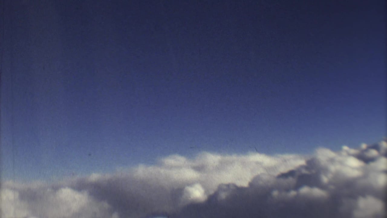 Blue sky above a thick bank of white clouds, with soft grain and film wear.