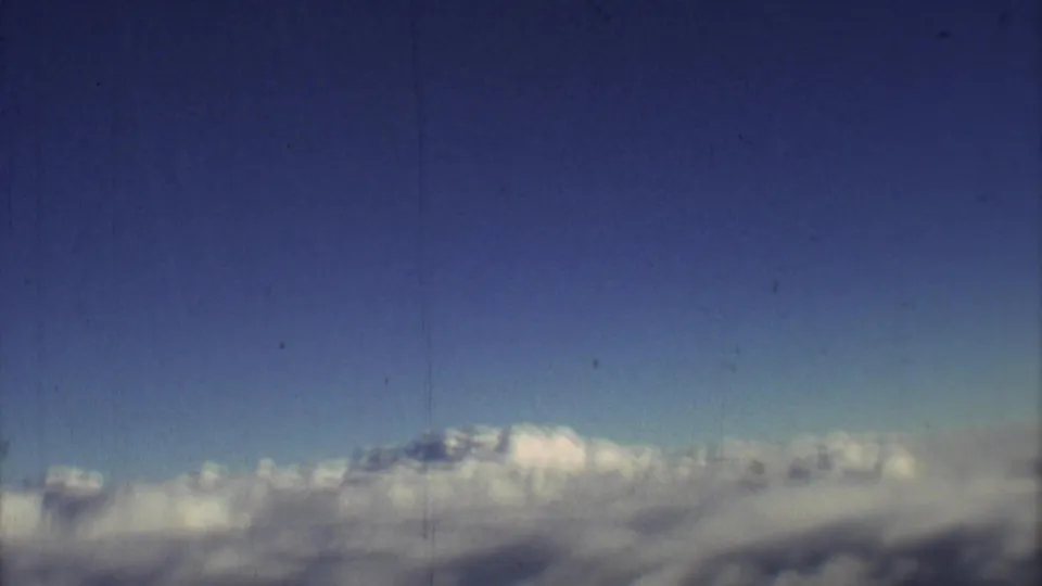 A 1973 8mm frame looks across distant clouds and blue sky from above the weather during an airplane flight.