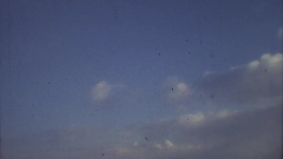 Grainy 1973 8mm footage shows scattered clouds and open blue sky from a passenger-like aerial viewpoint.