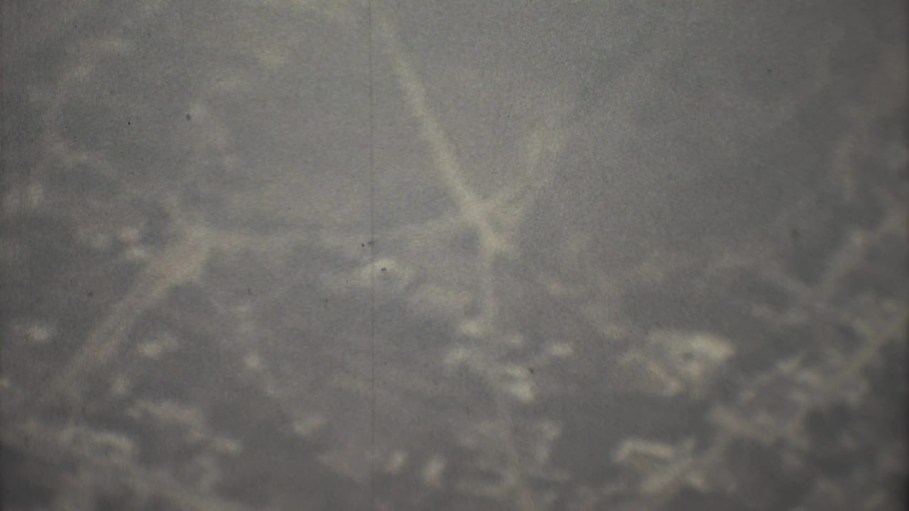 Hazy aerial view with indistinct ground texture and heavy 8mm grain.
