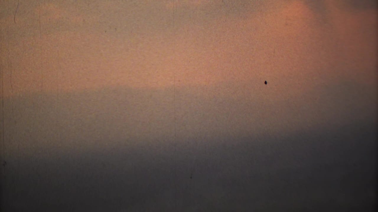 1973 Mexico City home-movie frame showing orange smog light, gray horizontal haze bands, dust, grain, and a small dark speck.
