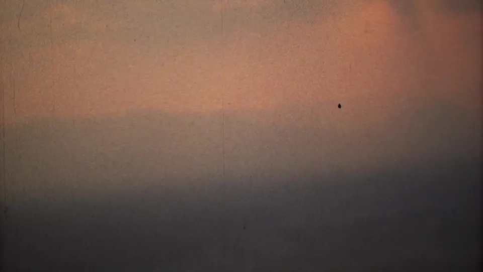 1973 Mexico City home-movie frame showing orange smog light, gray horizontal haze bands, dust, grain, and a small dark speck.