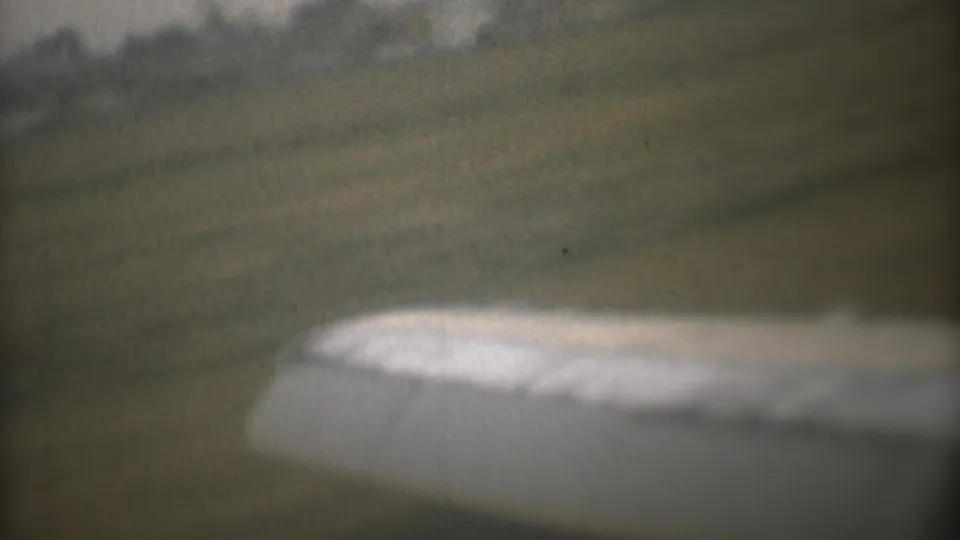 1973 8mm Mexico City travel footage showing a blurred aircraft wing beside a grassy airfield and distant treeline.
