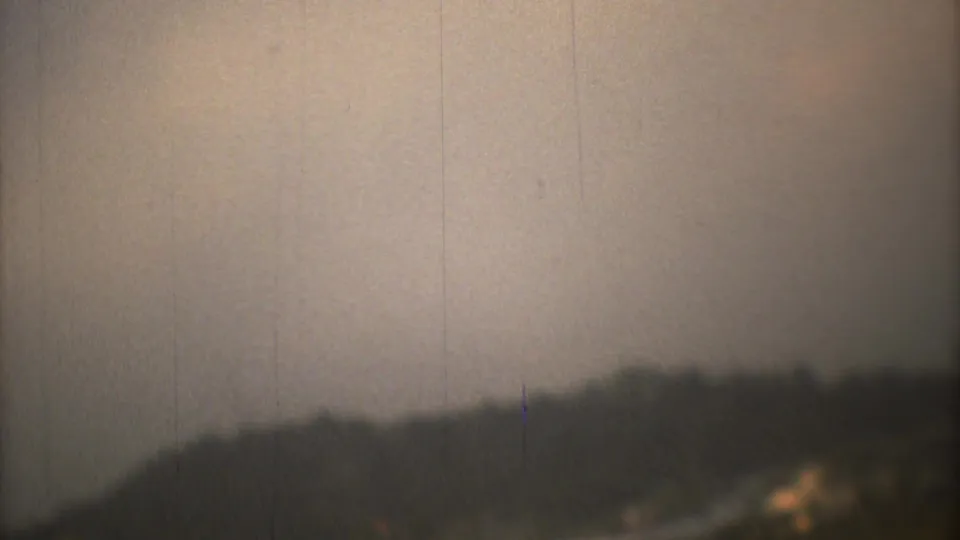 Mexico City 1973 8mm frame with a dark hillside, pale sky, and soft airfield edge seen from a moving aircraft.