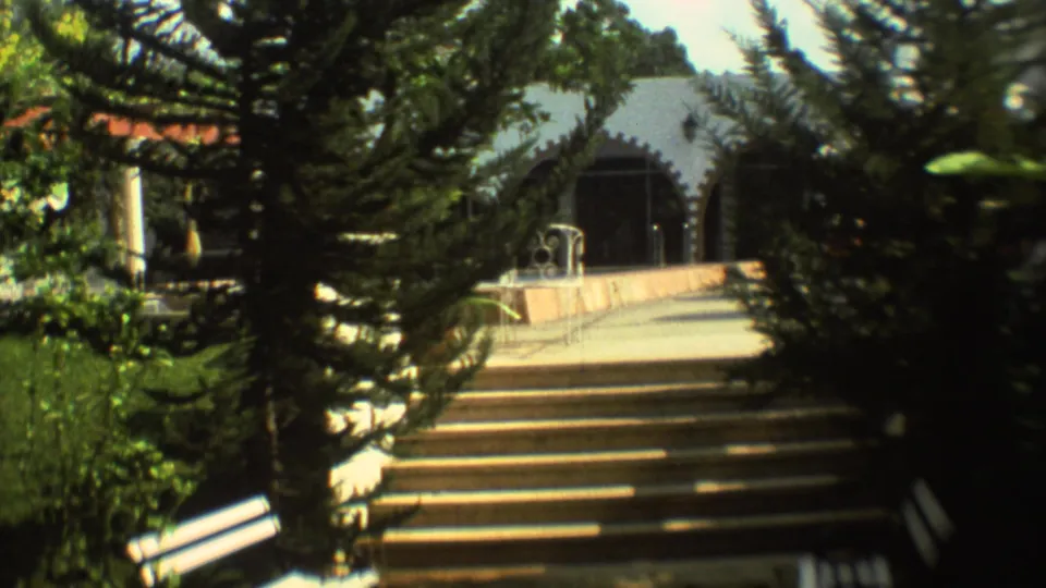 1973 Mexico City 8mm frame with trees, garden plants, broad exterior steps, and an arched building entrance.