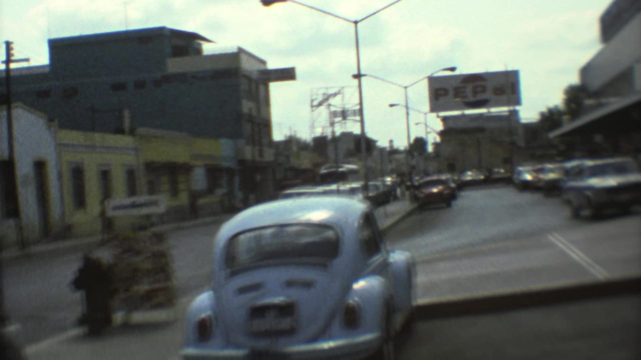 Blue Volkswagen Beetle on a city street near a Pepsi billboard and low-rise buildings.
