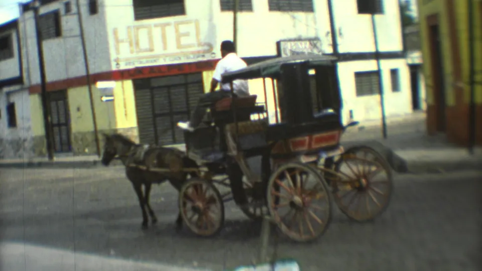 1973 Mexico City street scene with a horse-drawn carriage and driver passing storefronts and a large hotel sign.