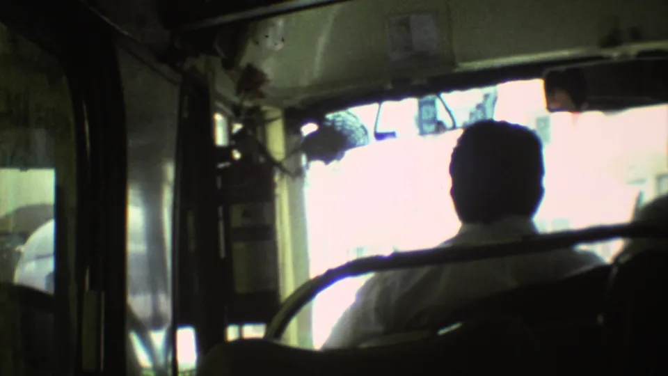 Interior bus view from 1973 Mexico City footage, showing a silhouetted passenger seated against a bright street-facing window.