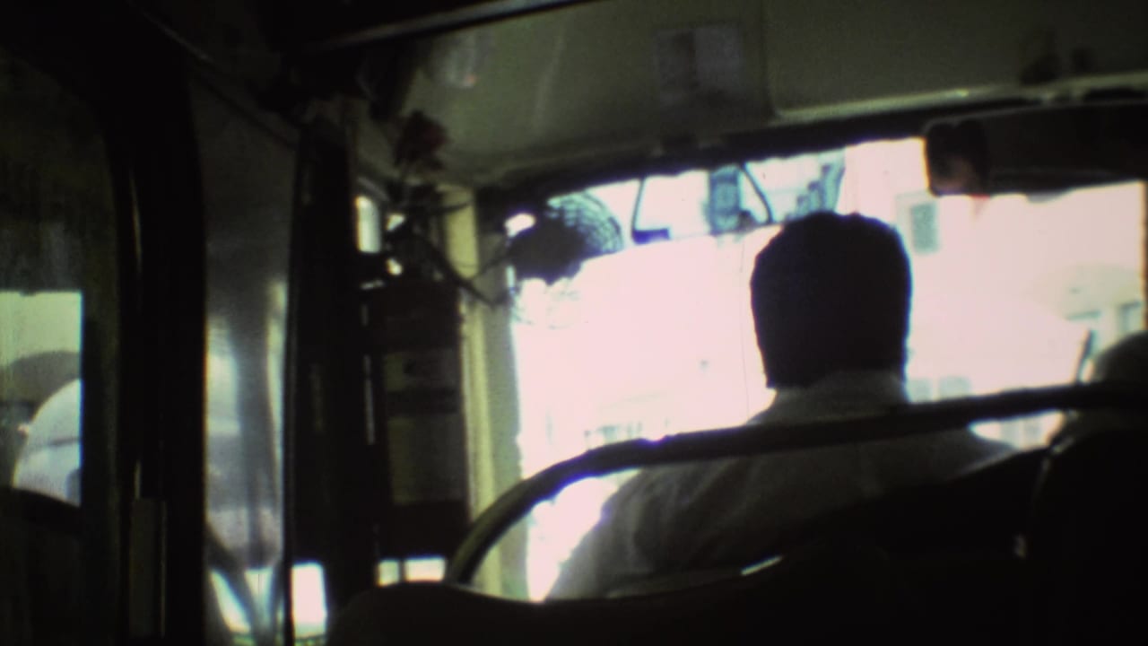 Bus interior seen from behind the driver with a bright windshield and metal handrails.
