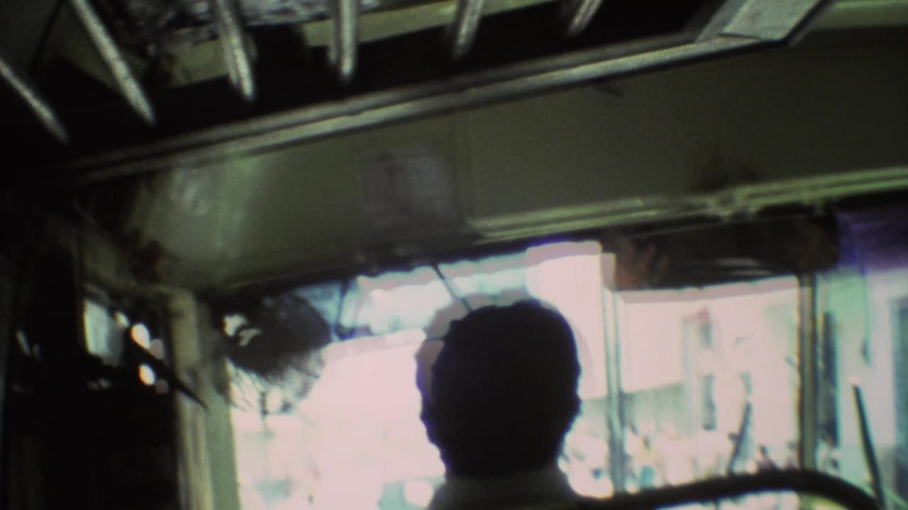 Passenger-view frame inside the 1973 Mexico City bus, with the front glass blown out by daylight and street shapes beyond.