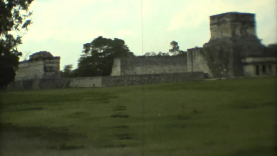 1973 Mexico City home-movie frame with open grass, a weathered stone landmark, and trees under a pale sky.