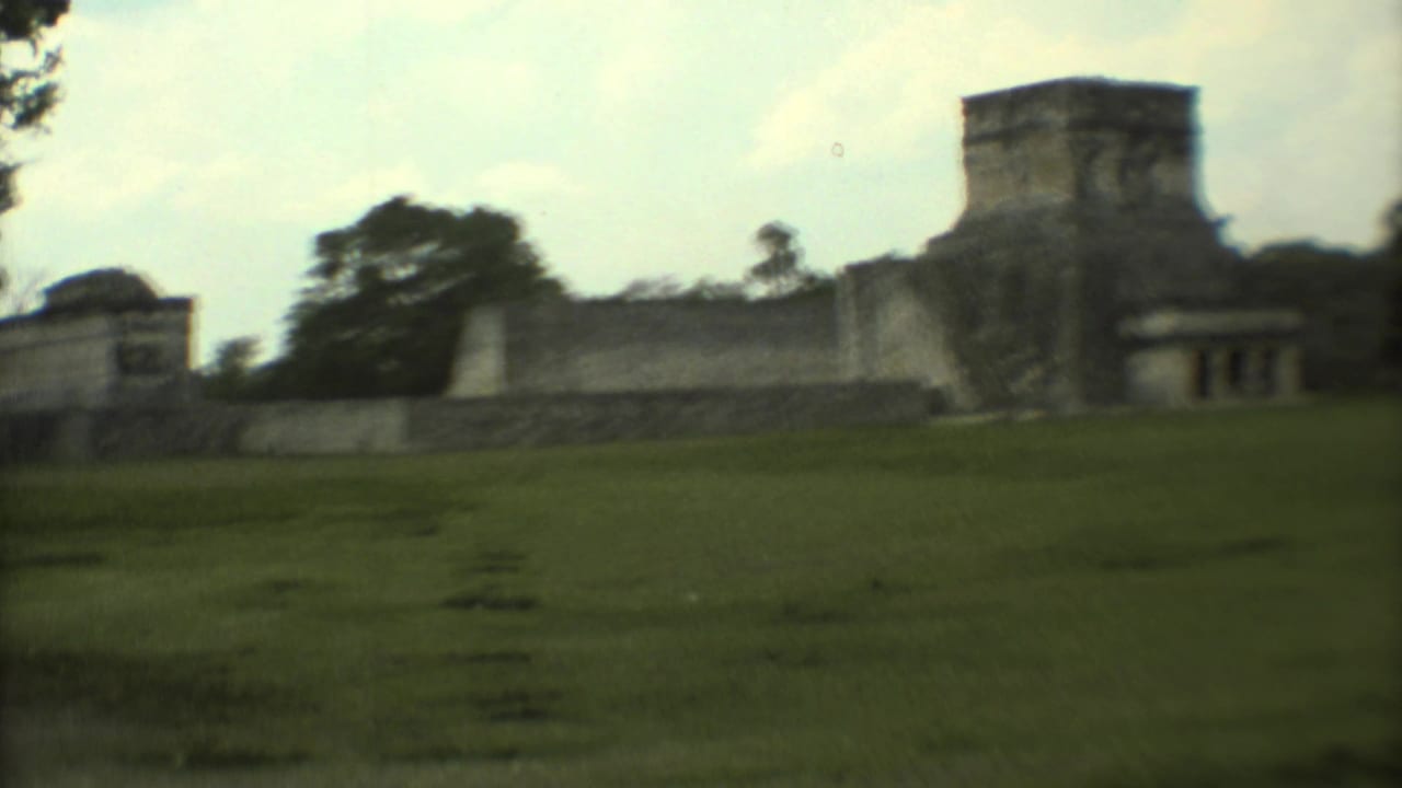 1973 8mm travel frame of stone ruins in Mexico viewed from a grassy area with trees and pale sky.