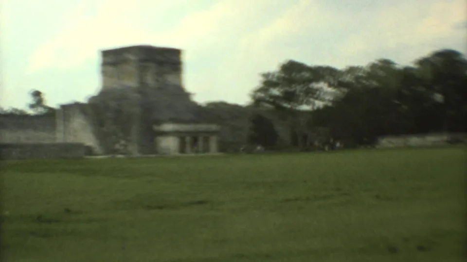 1973 8mm frame showing a panning view past stone ruins and trees at a Mexican archaeological site.