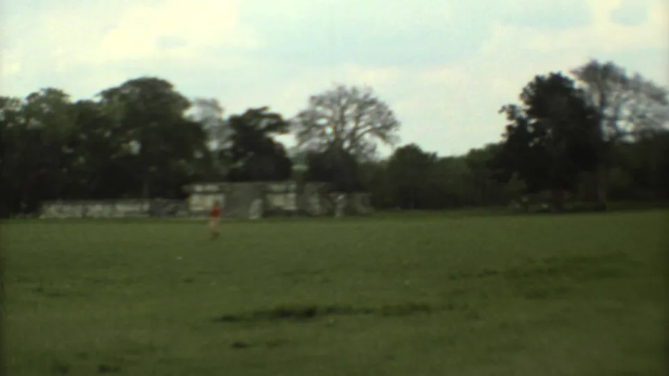 Soft 8mm frame from Mexico City in 1973 with a distant visitor in red near ruins across a broad green lawn.