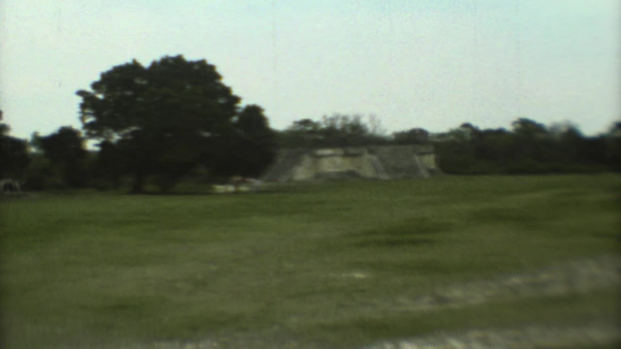 1973 8mm travel footage shows a distant stepped temple across grass at a Mexican archaeological site.