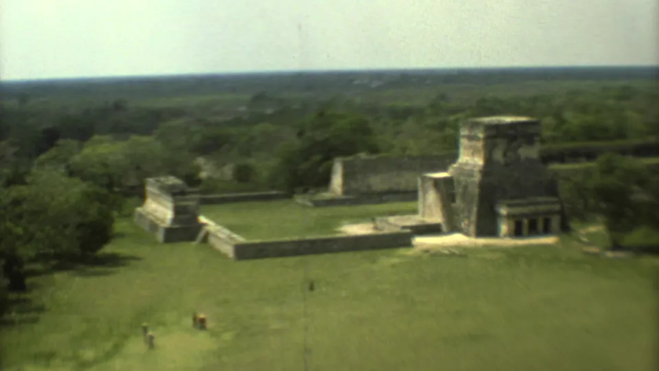 Aerial 8mm frame from Mexico in 1973 showing a stone ruin complex amid grass and surrounding jungle-like tree cover.