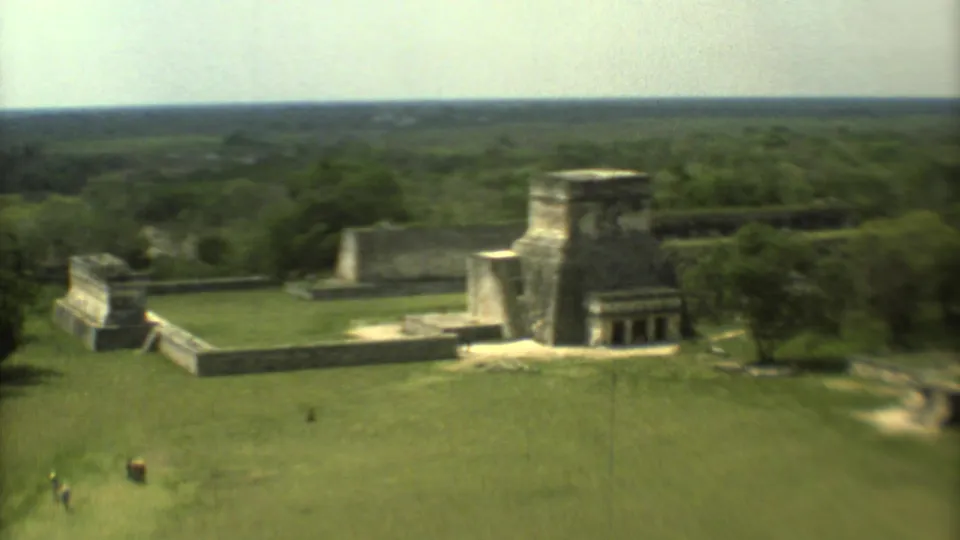 1973 home-movie aerial view of stone ruins in Mexico, with visitors crossing the grass and trees framing the site.