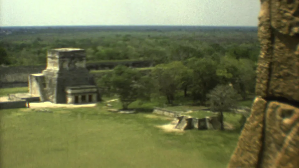 1973 Mexico home-movie frame with a stone temple, lawns, trees, and a carved stone pillar close to the camera.