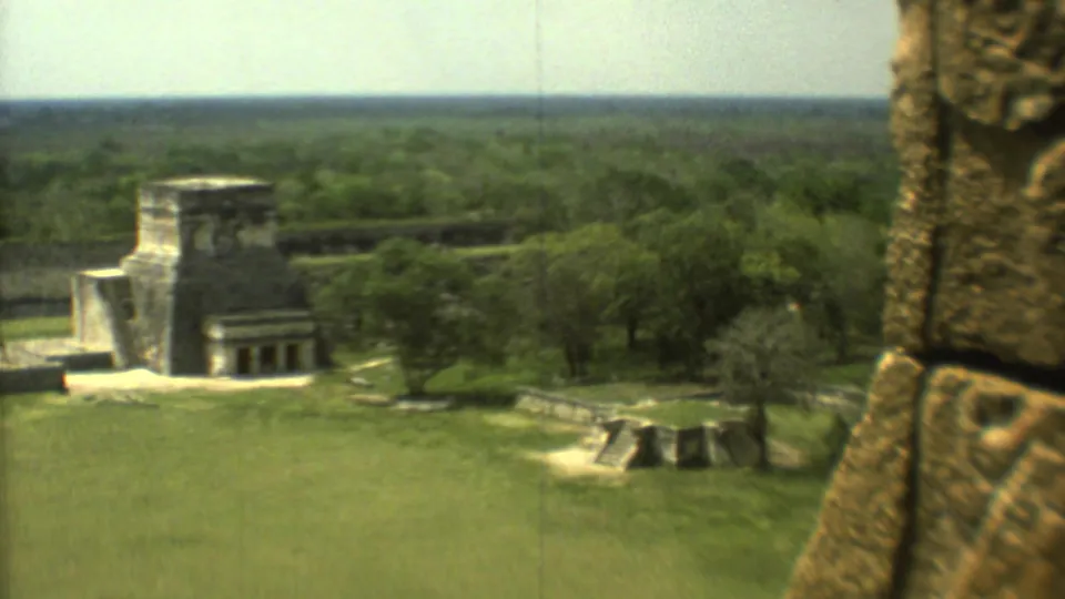 Visitor-shot 1973 8mm view of Mexican archaeological ruins with grass, trees, paths, and a close carved stone pillar.