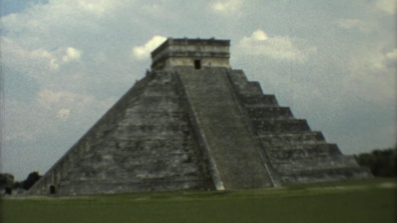Wide view of El Castillo pyramid with grass foreground and cloudy sky.