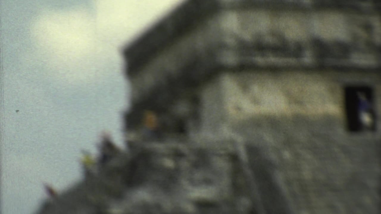 Soft, close view of the upper portion of a stepped stone temple against a pale sky.
