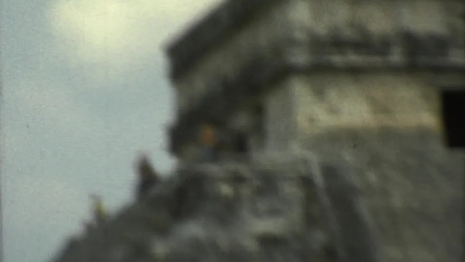 Soft 8mm frame of the temple summit and stair-stepped stone profile, with a distant visitor shape visible near the structure.