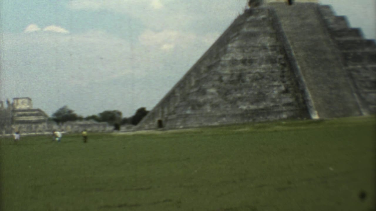 Handheld 1973 travel view of the pyramid grounds, with visitors small in the distance and ruins visible beyond the lawn.