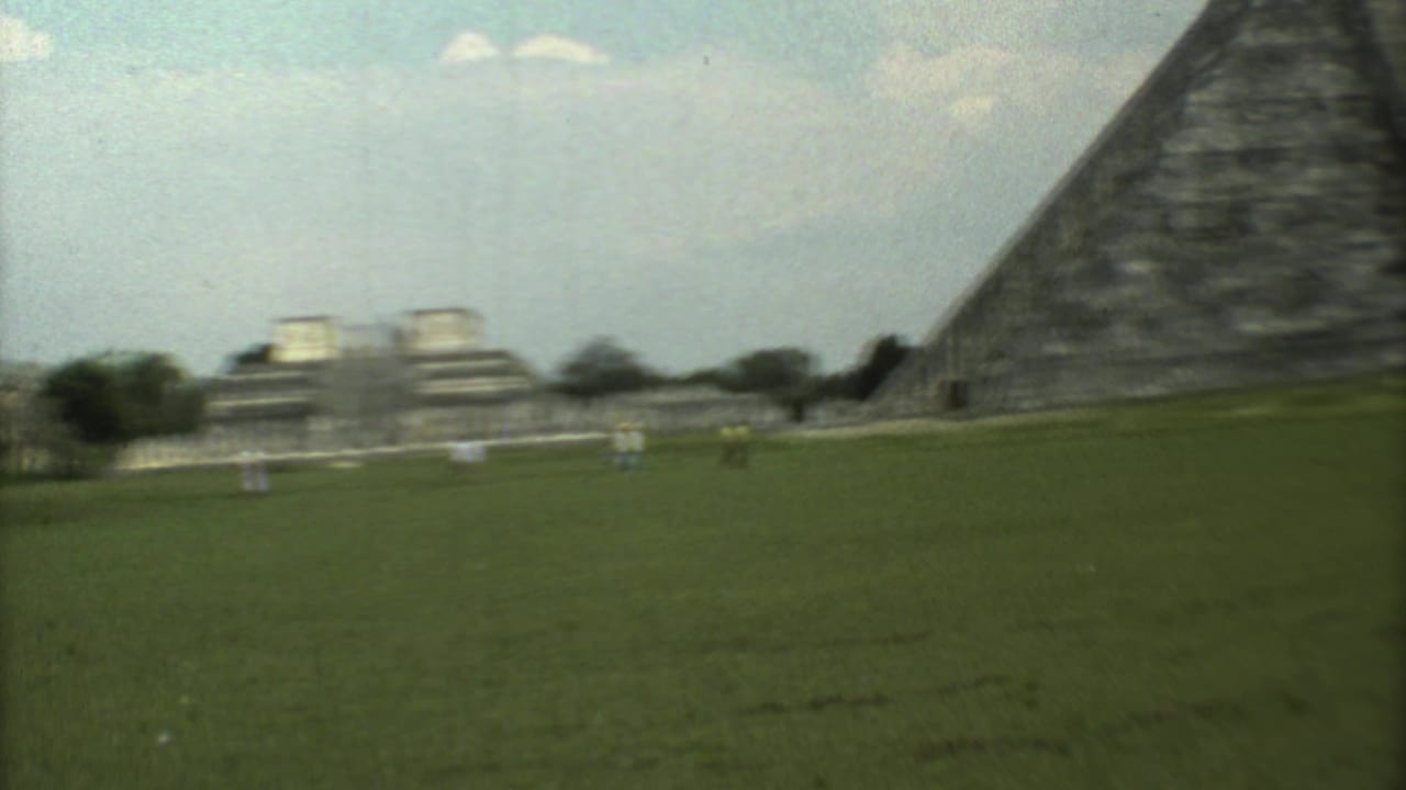Soft 8mm frame from the 1973 Mexico travel footage, showing the open site grounds, distant structures, and the edge of the pyramid.