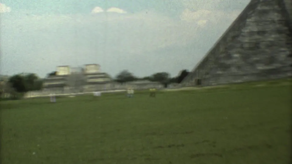 Soft 8mm frame from the 1973 Mexico travel footage, showing the open site grounds, distant structures, and the edge of the pyramid.