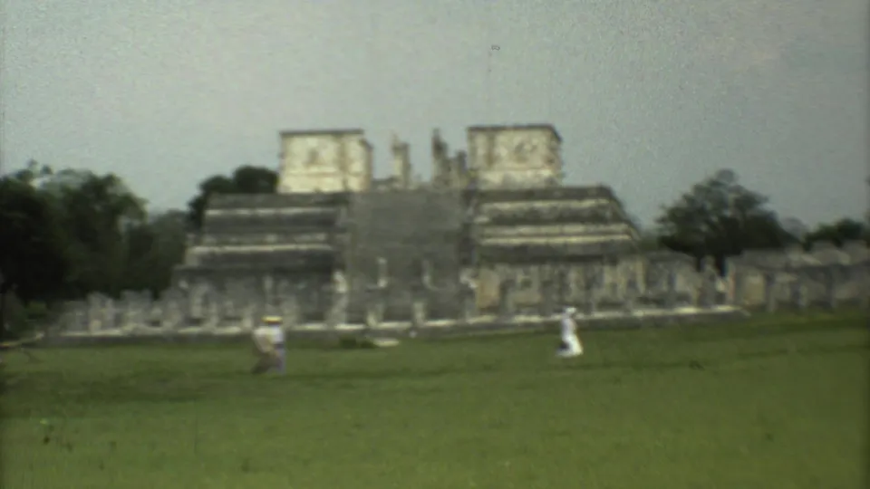 Soft 8mm frame of monumental stone structures and tourists moving across a grassy archaeological site in Mexico City.