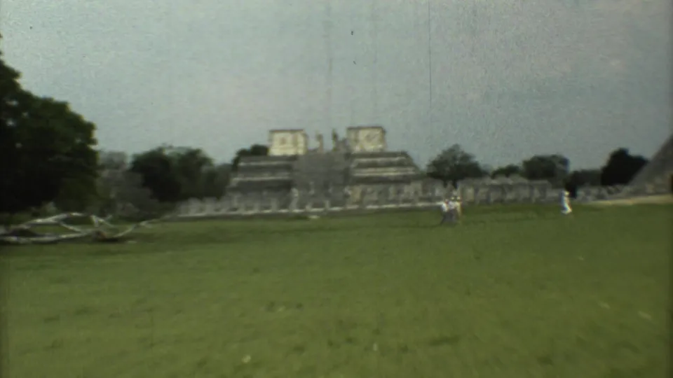 Wide 1973 home-movie view of tourists walking near ancient ruins in Mexico, with a pyramid-like structure partly visible at right.